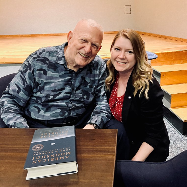 A young woman crouches next to a seated, older man.